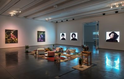 installation view of dimly lit room with furniture in the centre and paintings hung on the walls