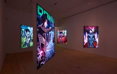 installation view of dimmed gallery space with four electronic images hung up, emitting light from them