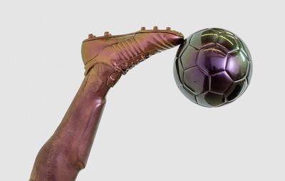 sculpture of a football player's leg, from the knee downwards, upside down and kicking a football with a football boot on their foot