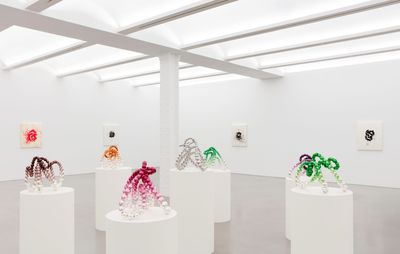 installation view of seven beaded sculptures of varying colours balanced on white pedestals
