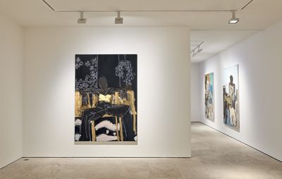 white gallery wall with large black and gold painting hung centrally and two paintings viewed from the side in the background
