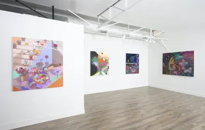 S photo of an art gallery, with white walls and a grey wooden floor. Four pieces of Guimi You's art hang on the walls in delicate pastel shades.