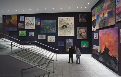 Staircase surrounded by two black walls covered in dozens of paintings in various sizes
