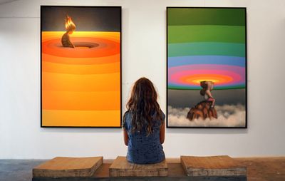 Two paintings displayed in a gallery, a person sits in front of them 