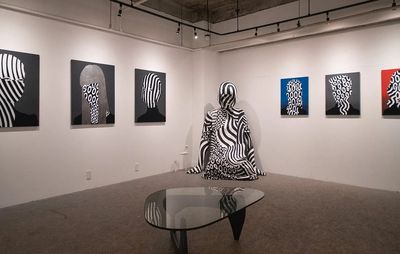 an installation view of six striped portraits hung on two walls with a large monochrome sculpture set between them
