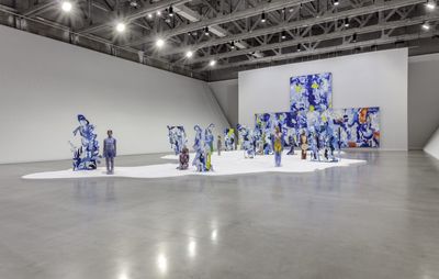 installation view of enormous exhibition space with numerous life-like sculptures of humans and large colourful, abstract canvases