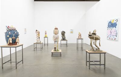 installation view of white walls with seven sculptures of varying sizes placed on top of tables, with several paintings hung on the walls