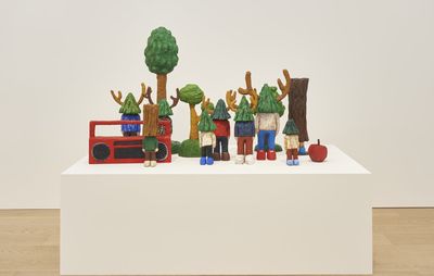 A group of sculptures of trees, figures with tree heads and a radio stand on a white block.