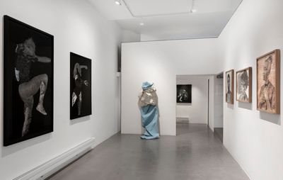 Installation view of paintings hanging on two walls by varying artists and a life-size sculpture by the far wall