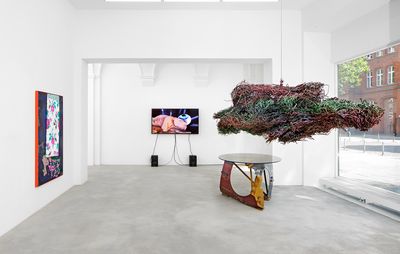 installation view of room with one screen hung on a wall, a painting on another, an artistic table and an installation hanging from the ceiling like a cloud