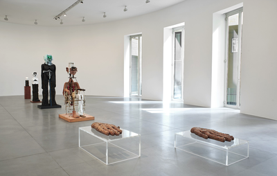 installation view of four sculptures lined up in a room, behind two clear tables which each hold a sculpted hand