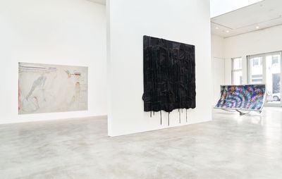 an installation view of a large black painting hanging on a white wall and dripping down out of the frame