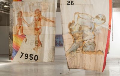 installation view of two thin pieces of fabric hanging from the ceiling with figurative paintings on them
