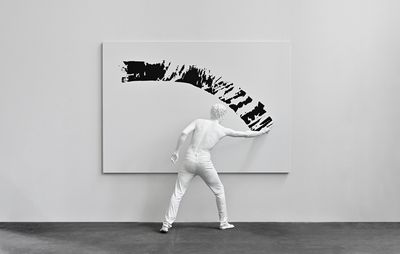 installation view of a white sculpture of a man spreading black paint across a white canvas