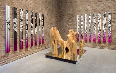 installation view of two seperate paintings, each split into eight vertical columns, with a large wooden sculpture on a plinth in the centre of the room