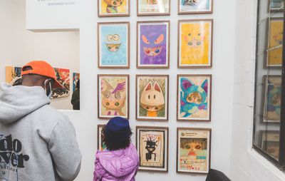 a child and a man looking at a selection of framed works by Ryol hanging on a wall