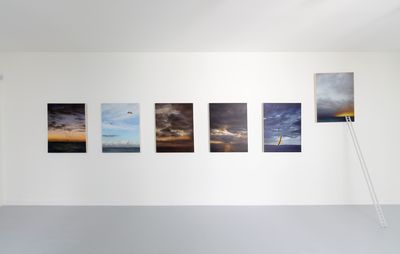 installation view of six paintings of the same size hung on a wall, with a small ladder reaching up to the far right painting that is raised above the others
