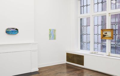 installation view of three small paintings by different artists hung on white walls and a window frame