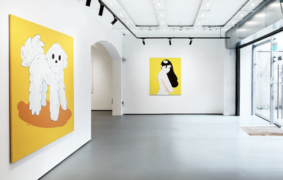 Yellow graphic paintings hang in white exhibition space