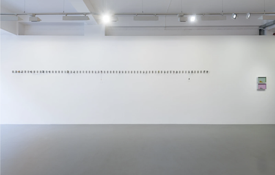 installation view of white wall with dozens of similar tiny artworks hung in horizontal alignment