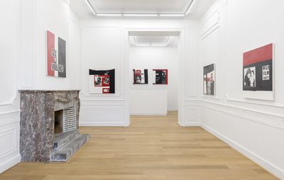 installation view of white walls with red, black and white paintings hung on them and a grey fireplace