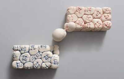 Two rectangular sculptures hung on a wall of round, crying faces all stuck together
