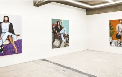 A photo of a gallery space with a concrete floor and white walls. Three large Evgen Čopi Gorišek paintings hang on the walls, with bright coloured backgrounds and signature portraits with simply drawn faces