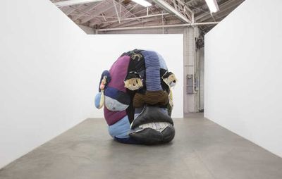 installation view of a large patchwork head placed in an empty white-walled room