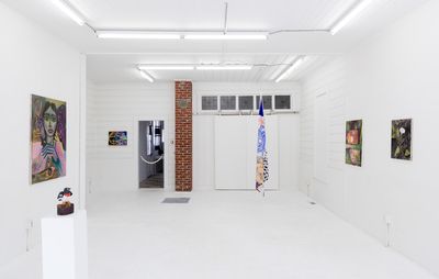 A photo of a white gallery space, with white brick walls and a white floor. Four pieces of art hang on the walls