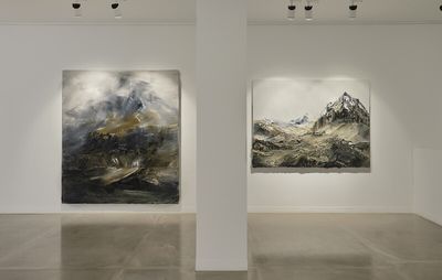white walled gallery space with two mountain paintings separated by a freestanding white column 