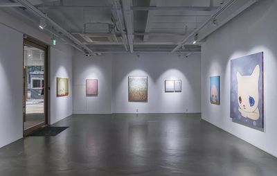 installation view of a large grey room with various spotlighted artworks hung up