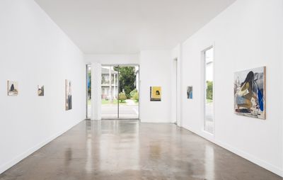 installation view of a large light gallery space with various sized paintings hung around it