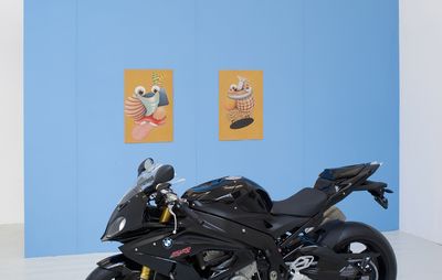 two drawings hung on a blue wall behind a motorbike