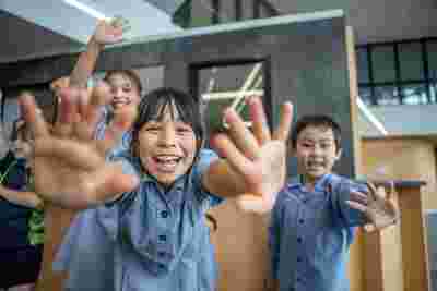 Children in school uniforms smiling and reaching towards the camera, with a playful and cheerful expression.