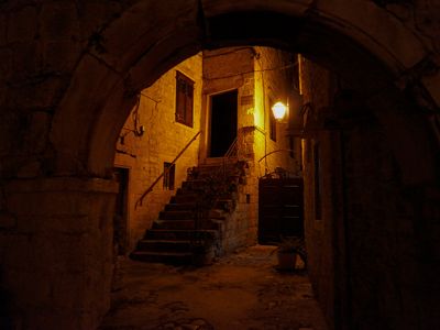 A lamp illuminates a staircase through a stone archway at night