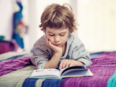 Junge liegt bäuchlings auf dem Bett und schaut in ein Buch