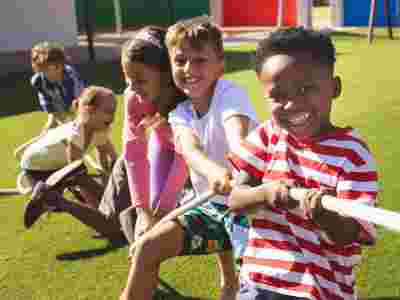 Children smiling and playing tug-of-war on green grass, enjoying a sunny day outside.