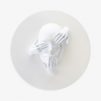 a white gloss sculpture of a face emerging from a circular backboard
