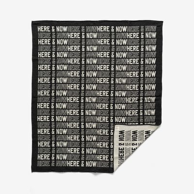 a monochrome blanket with text printed on it reading 'Here & Now'