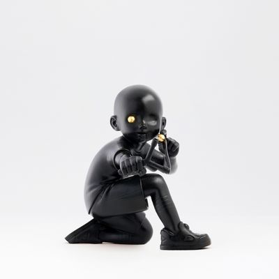 Black sculpture of kneeling boy with a slingshot and a golden eyeball