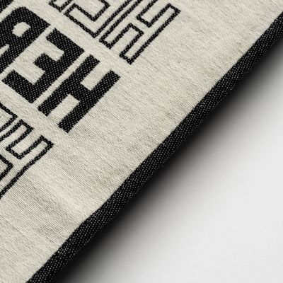 a close-up of a monochrome blanket with text printed on it reading 'Here & Now'