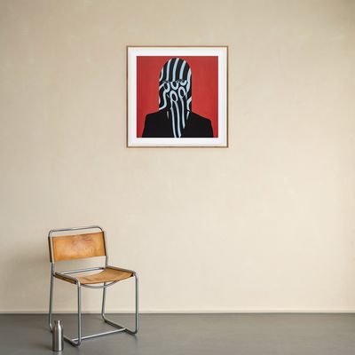 a framed print edition hanging on a white wall above a wooden chair