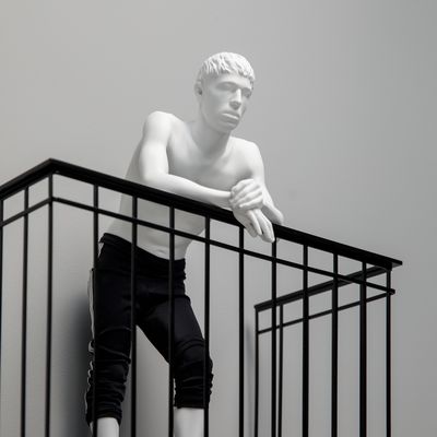 clothed resin figure leaning over metal balcony railing, looking into the distance