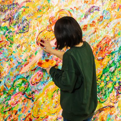 Ayako Rokkaku adding details to a figure in the centre of a large colourful painting