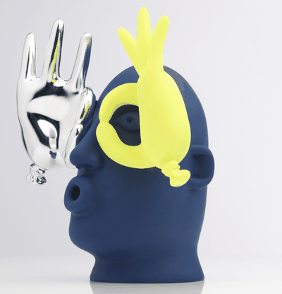 vinyl sculpture of an expressive cartoon face with yellow and silver hands – side view