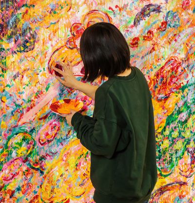 Artist paining on canvas with their hand, holding a paper bowl in the other hand