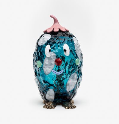 blue glass sculptural character with gold feet and a smiling face
