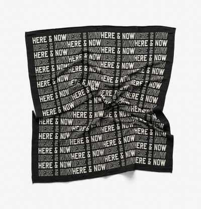 a monochrome blanket with text printed on it reading 'Here & Now'