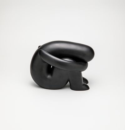 Black sculpture of a figure curled up sitting on the ground