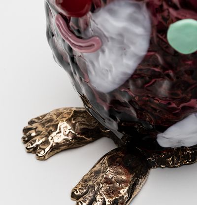 detail of a violet glass sculpted character with gold feet and a smiling face